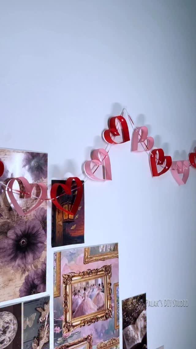Red and pink paper heart garland hanging above a wall photo collage.