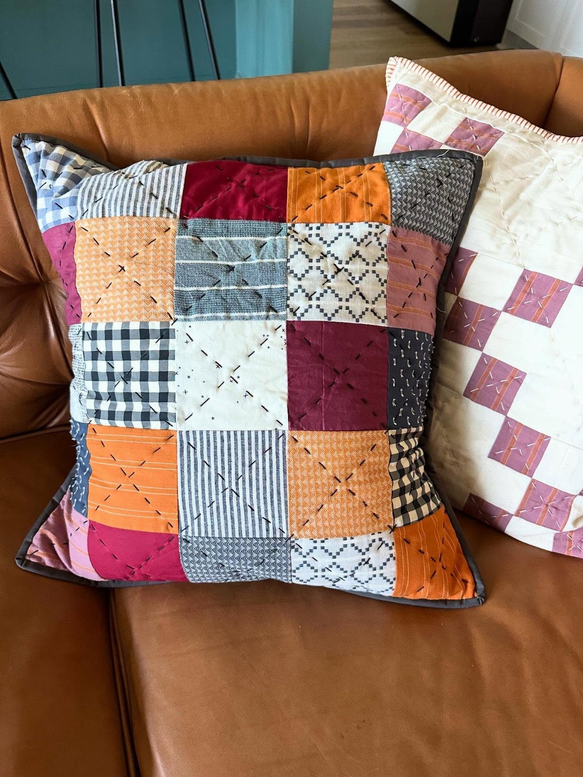 Patchwork throw pillows with colorful fabric squares on a brown leather sofa