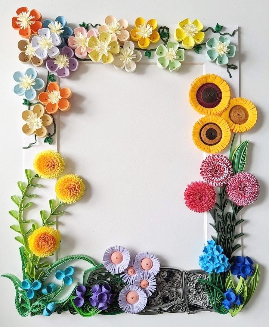 White picture frame decorated with colorful quilled paper flowers and green leaves.