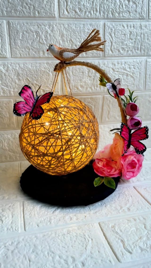 Woven twine spherical table lamp decorated with pink butterflies, roses, and a bird.