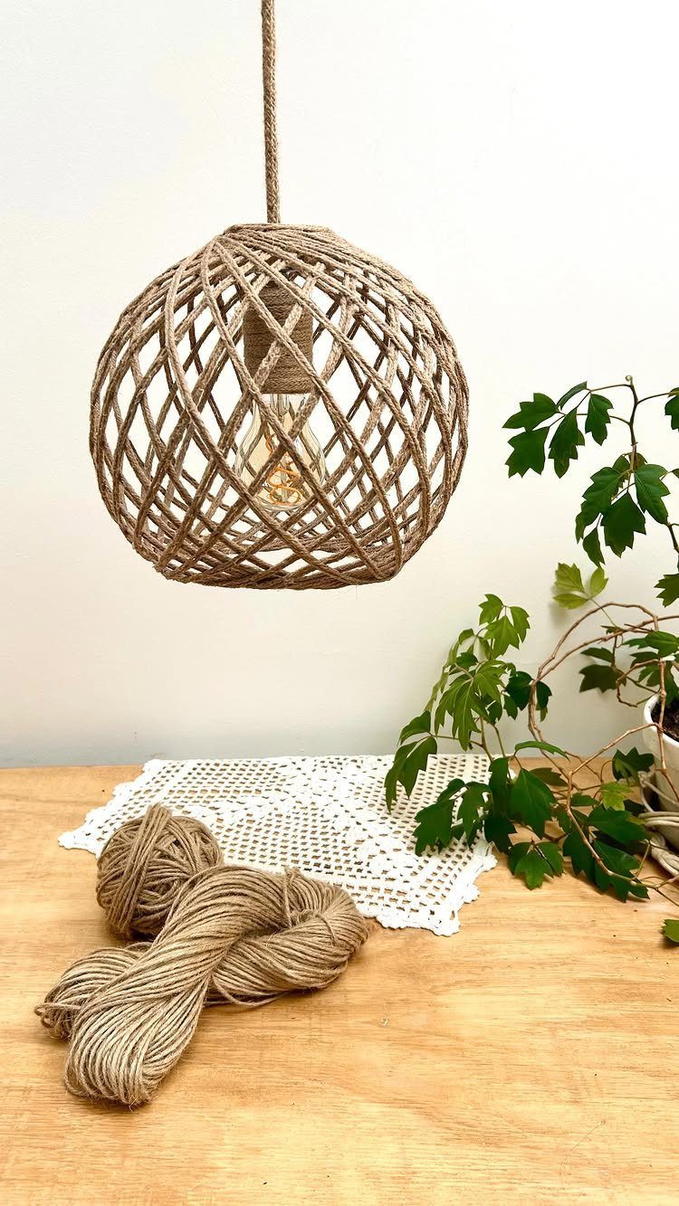 Woven rope spherical pendant lamp hanging over a wooden table with rope and plant