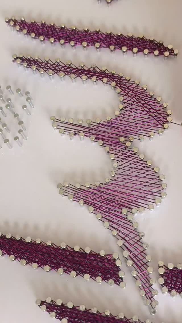 Purple string art woven between silver pins on a white background