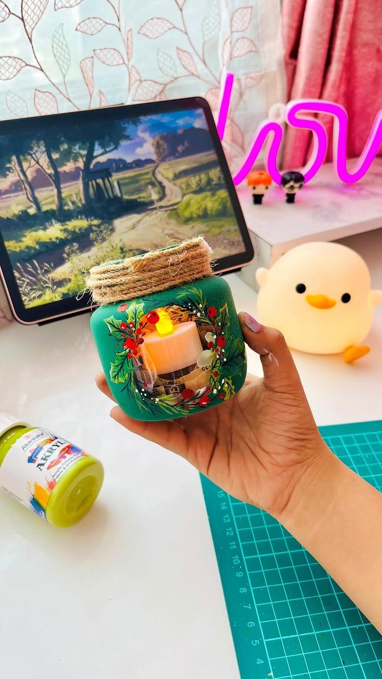 Green painted mason jar with floral art and twine lid held by hand