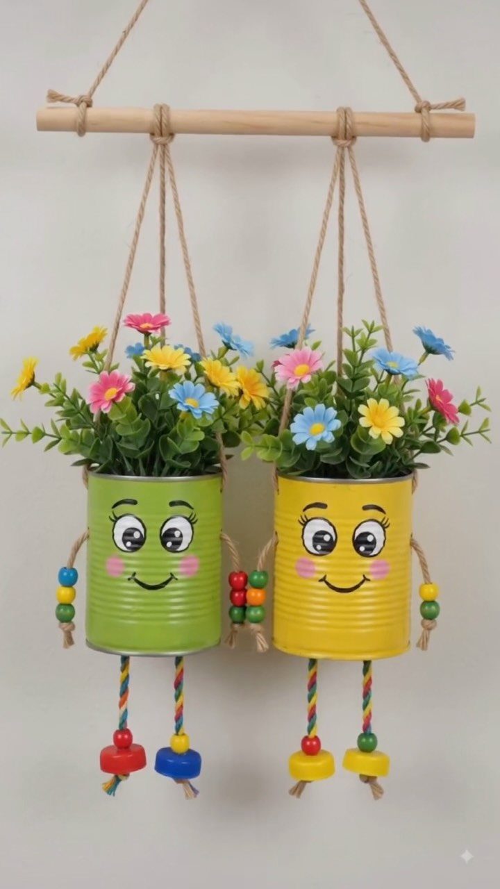 Two painted tin can planters with cartoon faces hanging from a wooden rod.