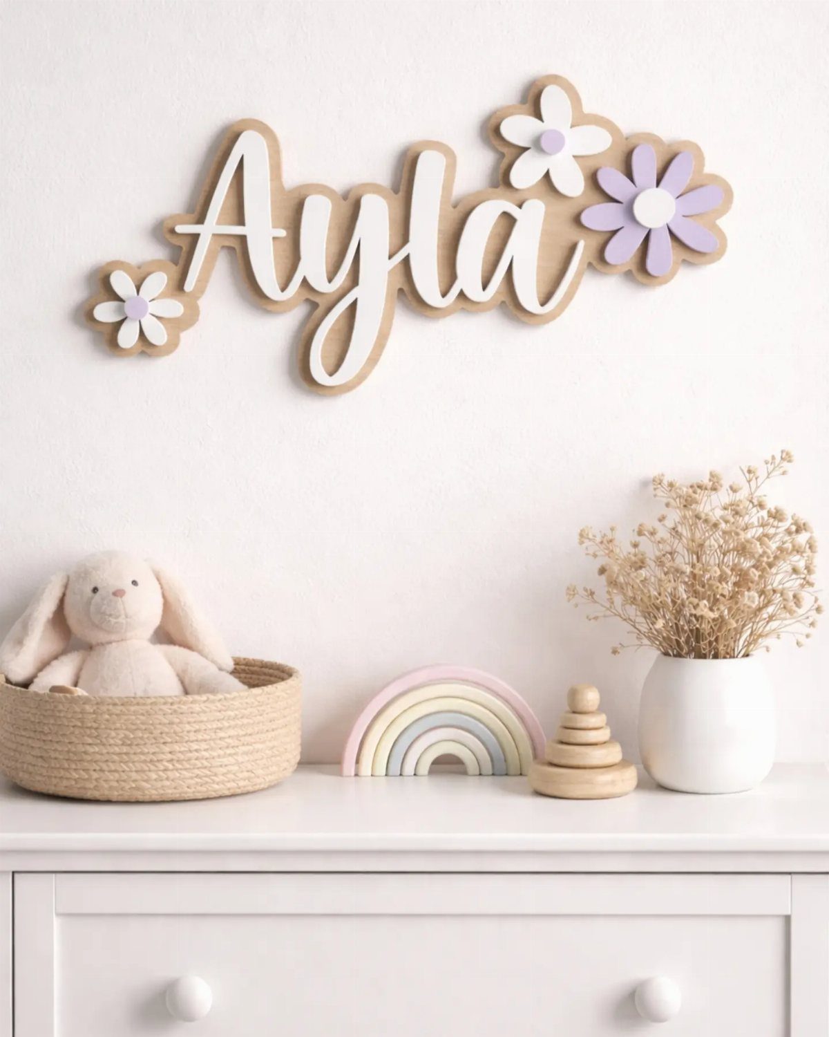 Wooden name sign Ayla with purple flowers on a white wall above dresser