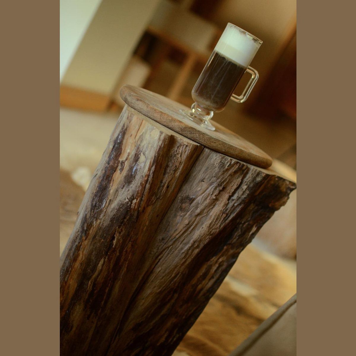 Tree stump side table with a flat wooden top holding a coffee glass.