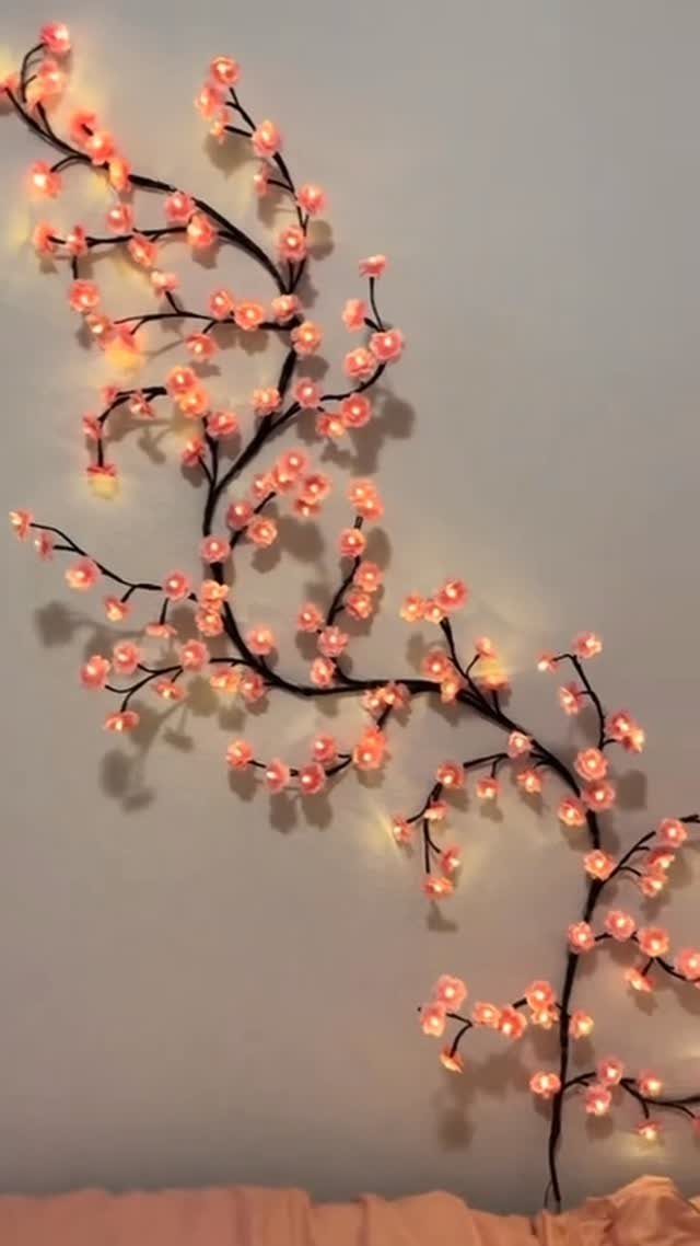 Glowing pink flower fairy lights arranged like a branch on a white wall