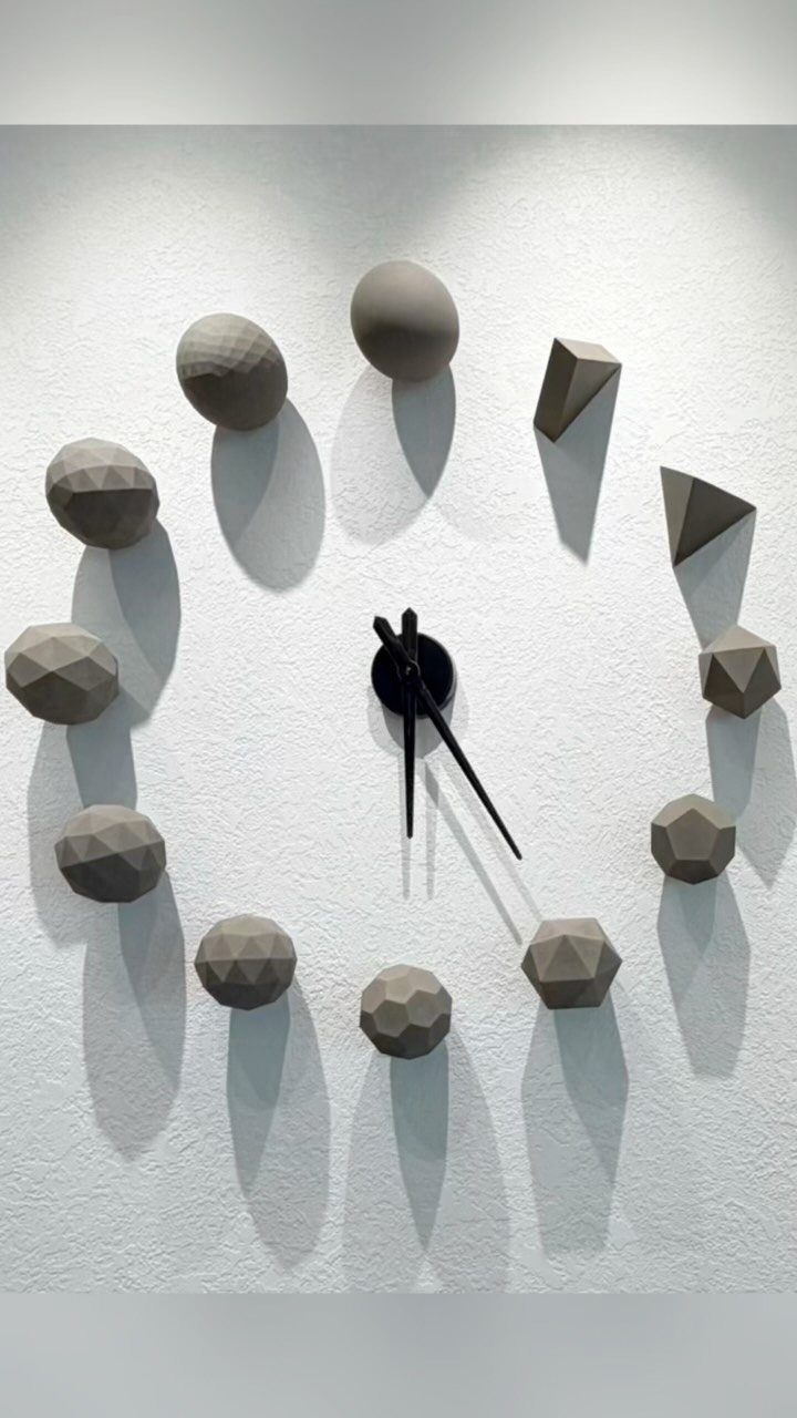 Geometric wall clock with grey polyhedral shapes as hour markers on white wall