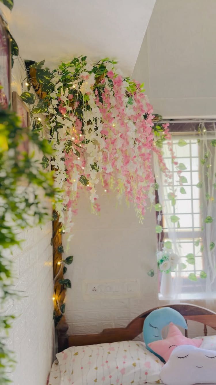 Cascading pink and white artificial flowers with fairy lights decorating a bedroom wall.