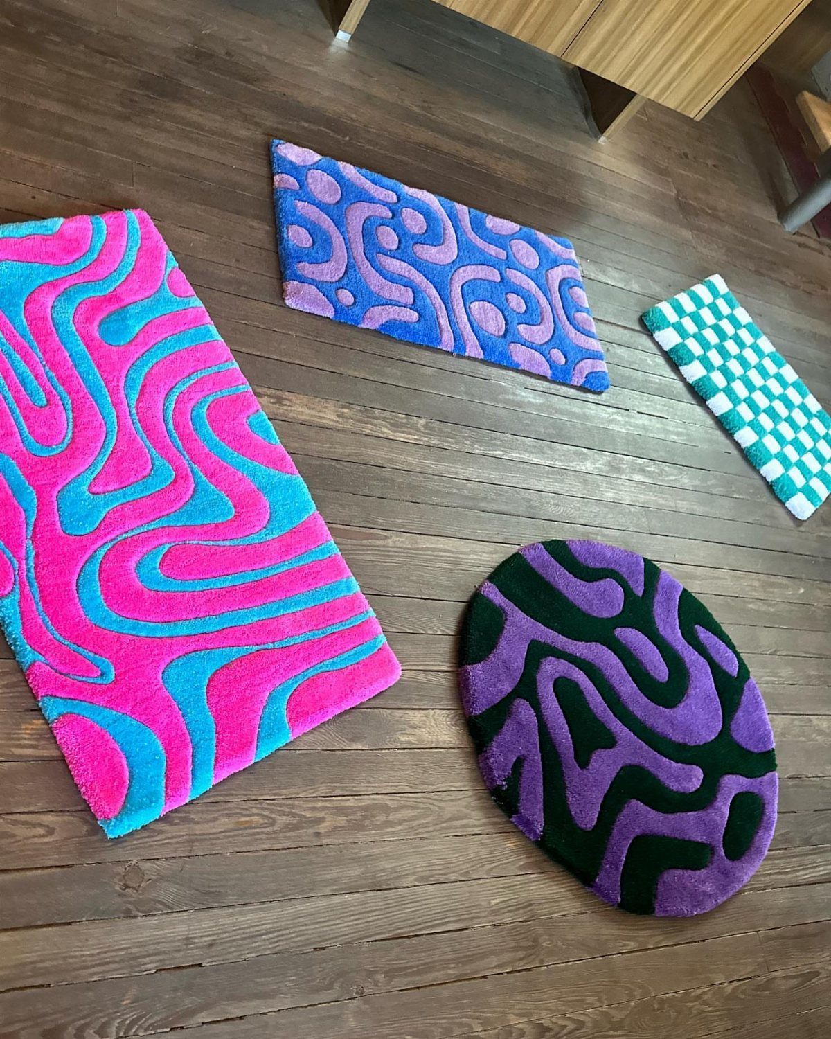 Four colorful tufted rugs with wavy patterns on a dark wooden floor.