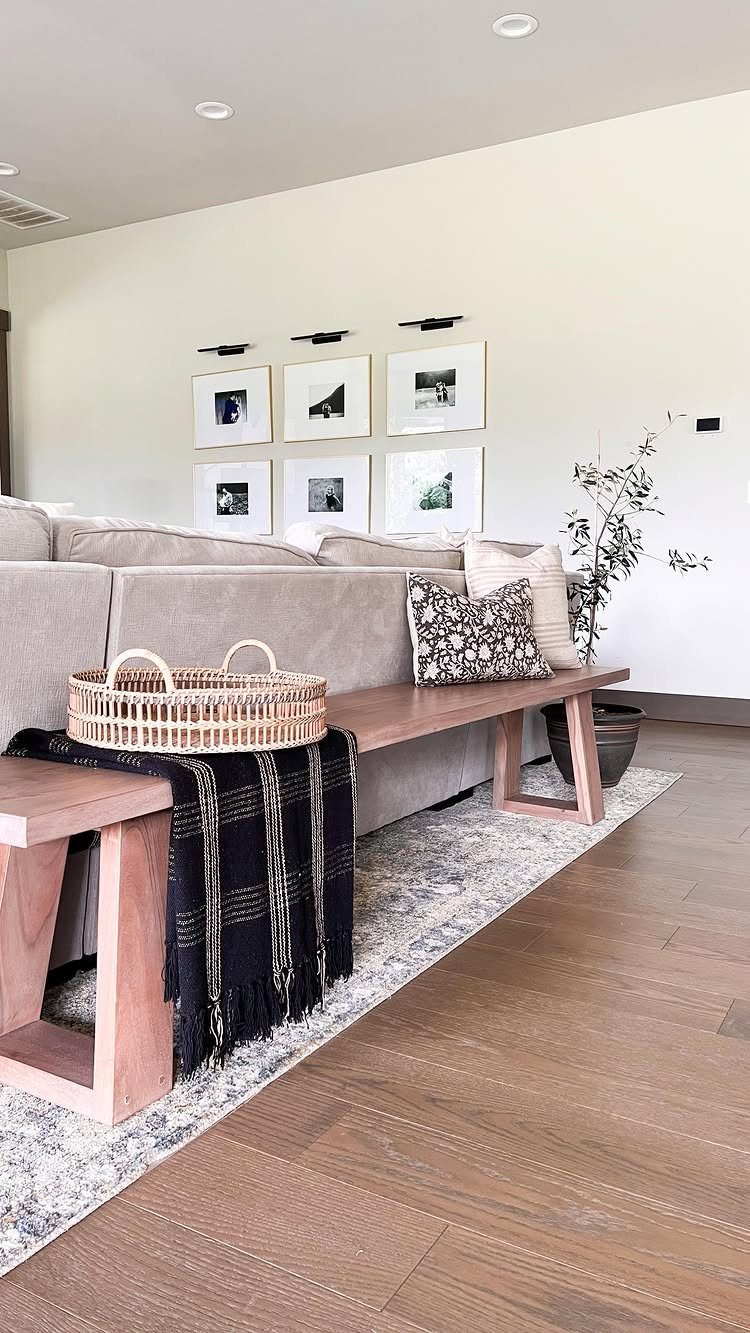 Grey sectional sofa with a wooden bench and framed photos on white wall