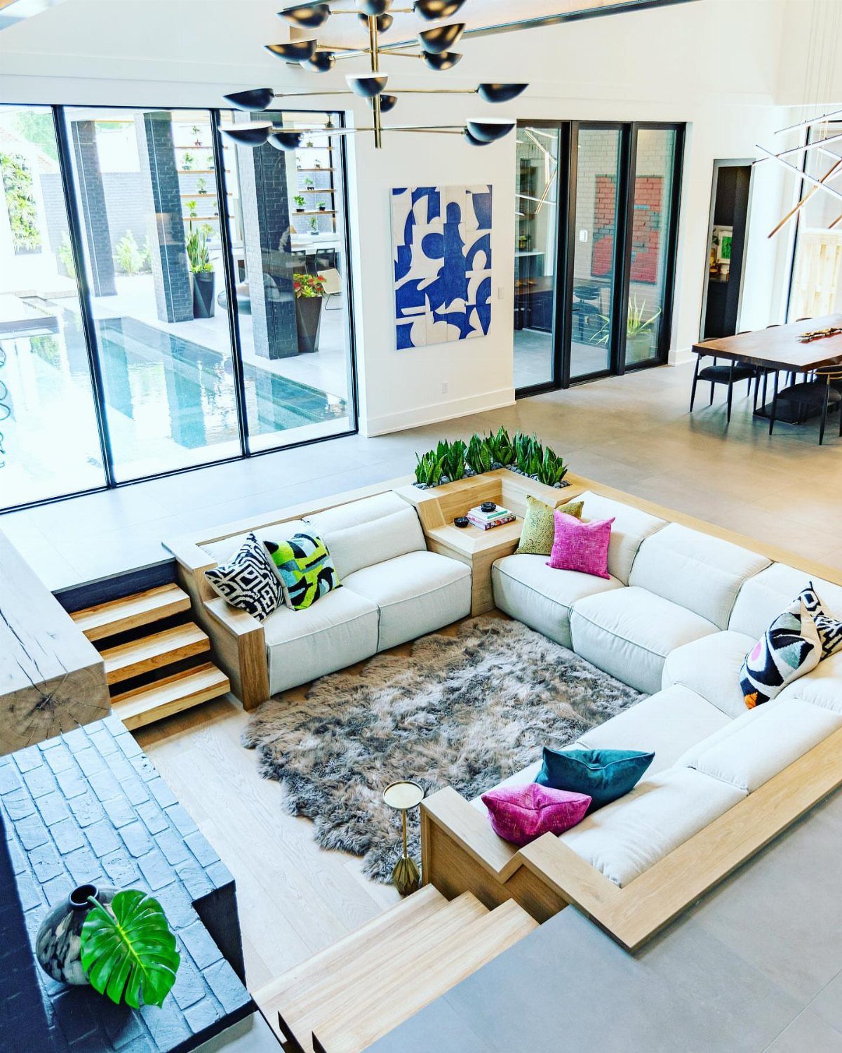Sunken living room with white sectional sofa, colorful pillows, and grey shag rug.