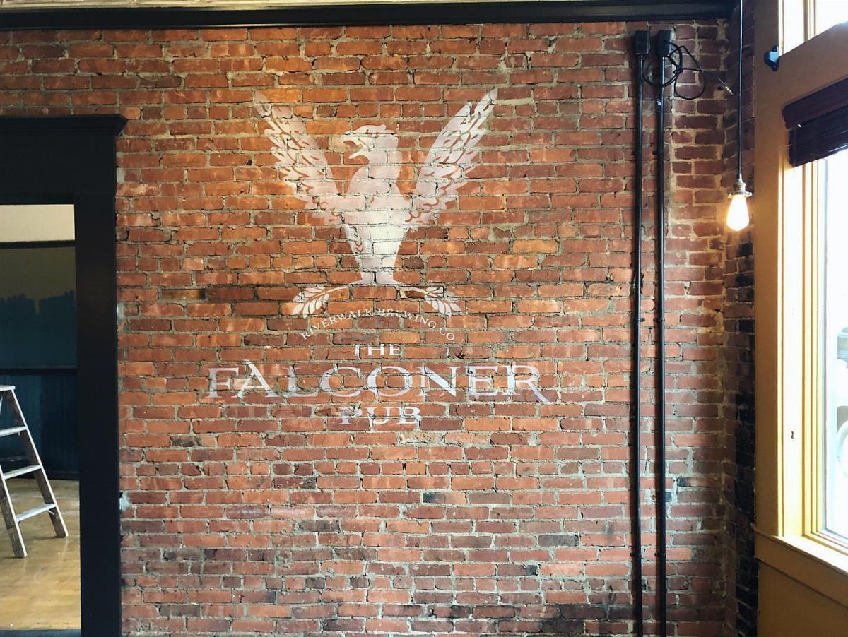 White falcon mural and text painted on a red exposed brick interior wall