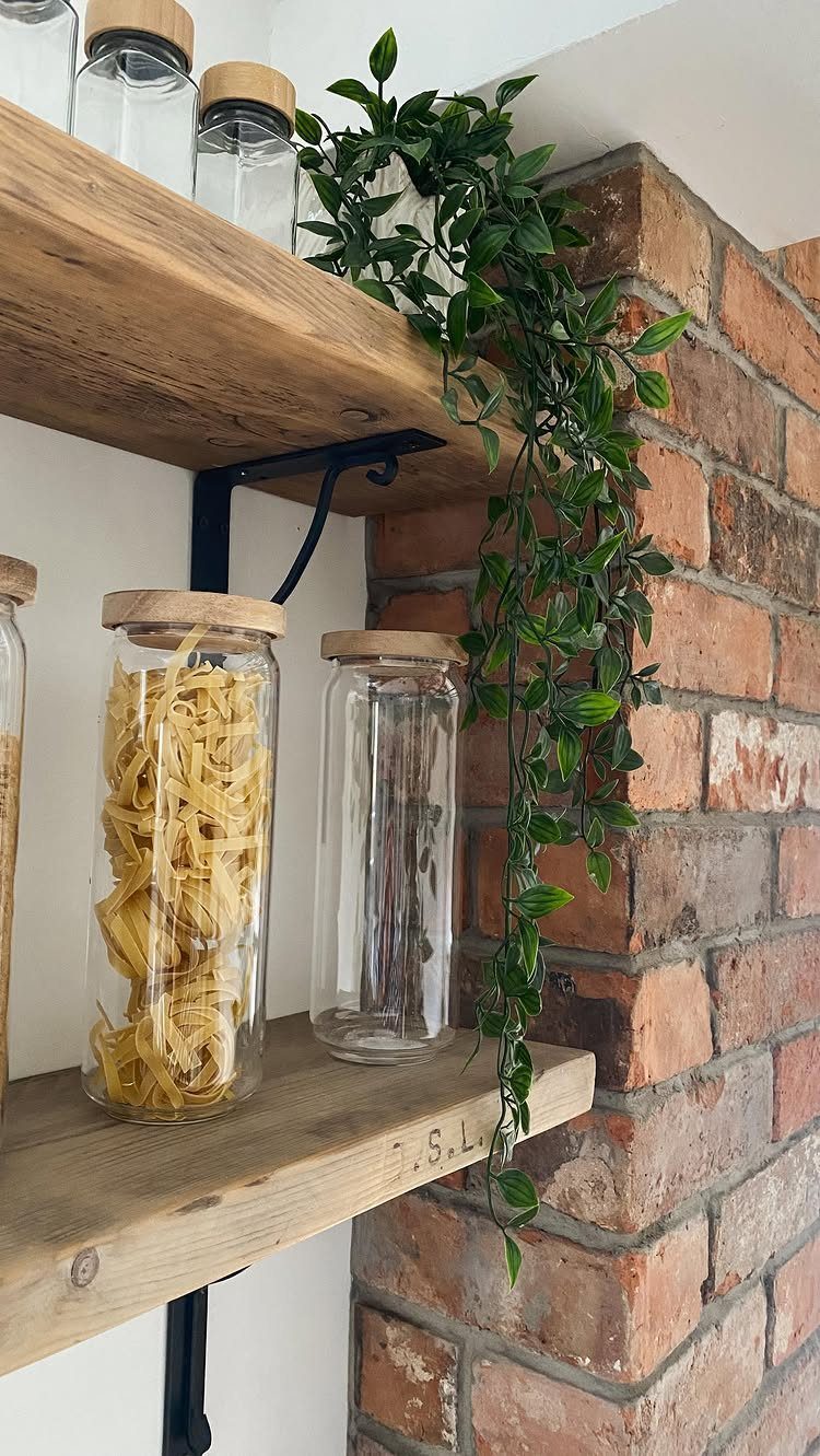Wooden shelves with glass jars and a green plant against exposed brick wall