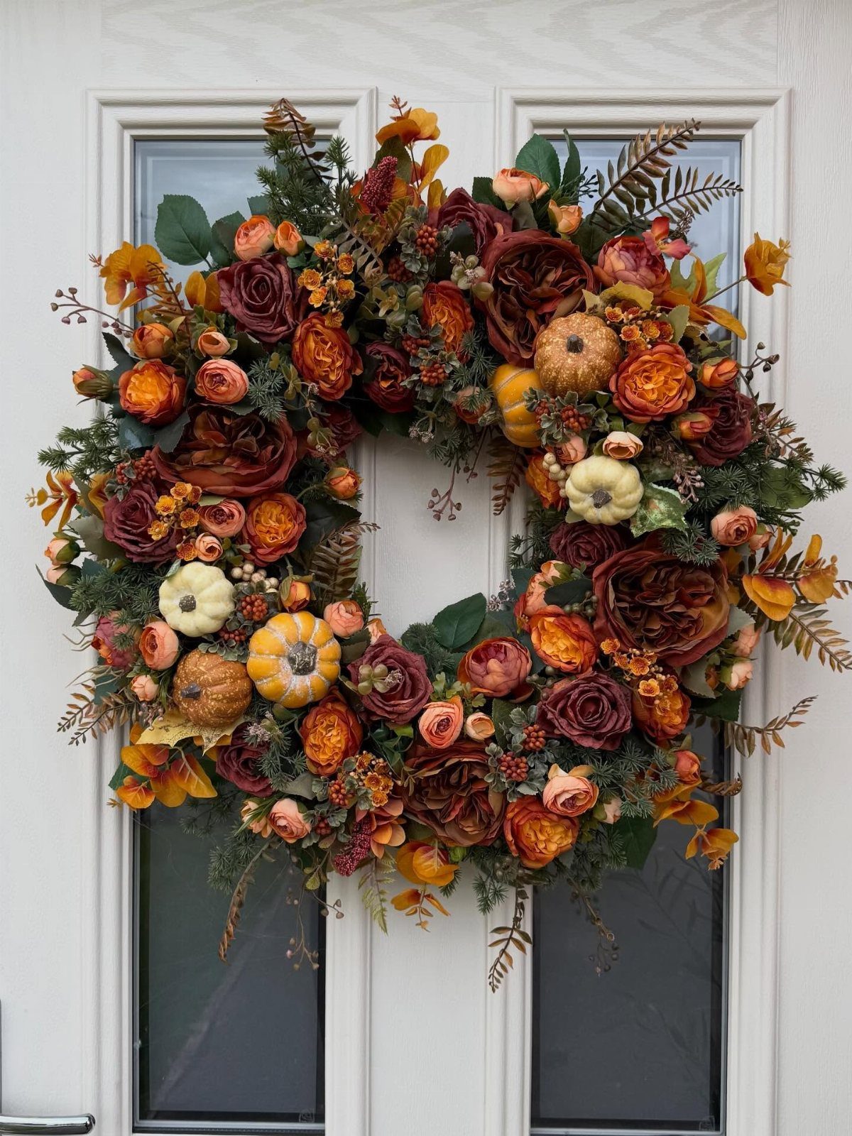 Autumn wreath with red roses and small pumpkins hanging on a white door.