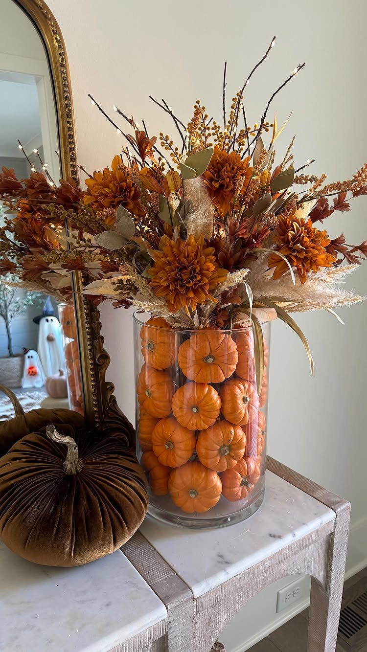Glass vase filled with mini orange pumpkins topped with autumn floral arrangement.