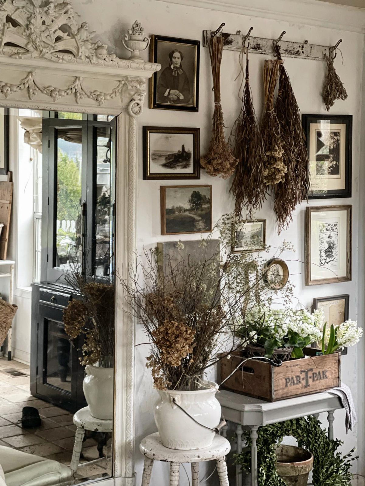 Vintage framed prints and dried herbs hanging on a white farmhouse style wall.