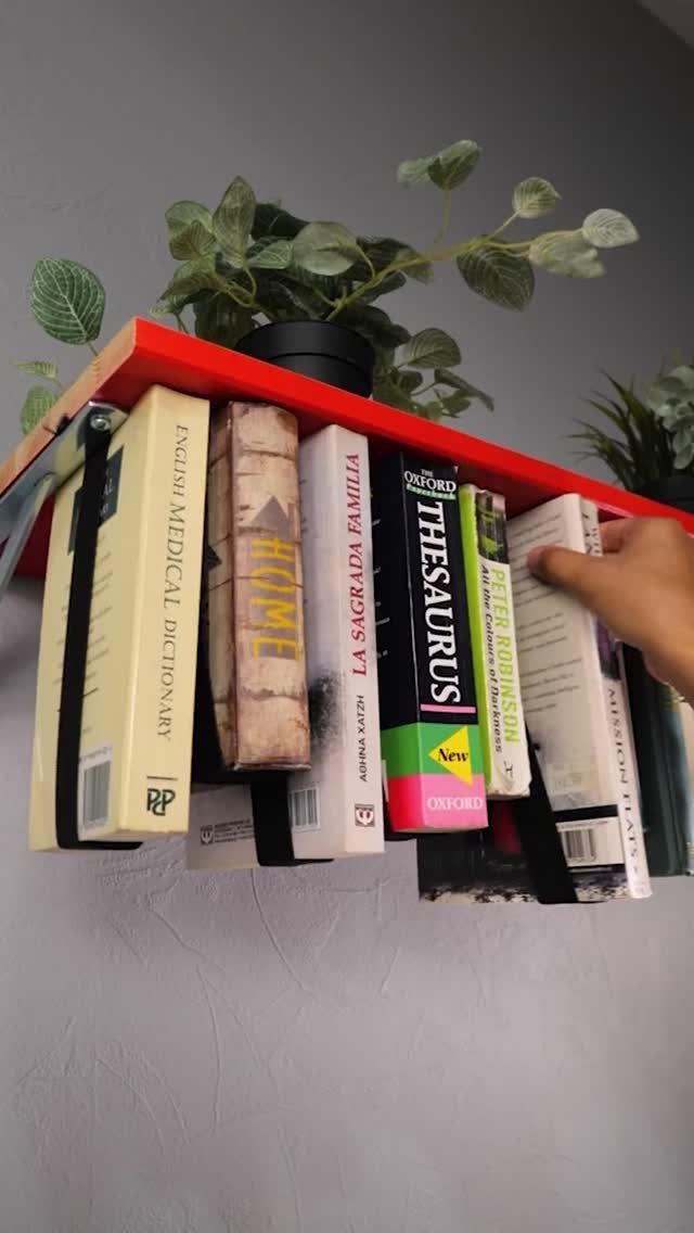Red floating shelf with books secured by straps and a potted plant on top