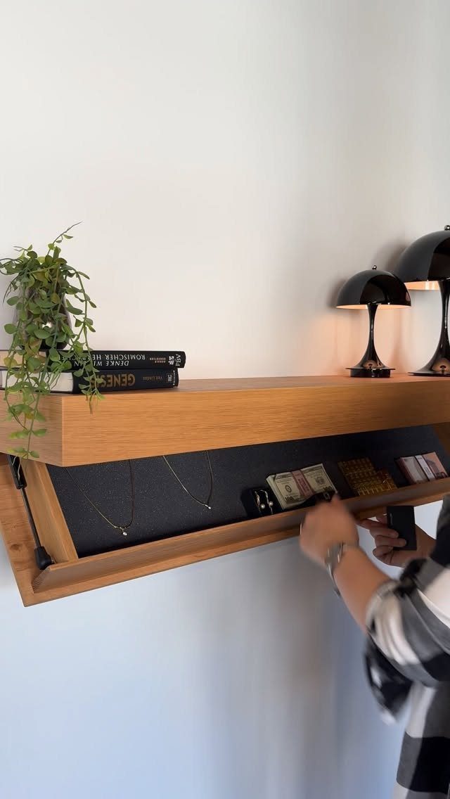 Wooden floating shelf with hidden compartment, books, and black lamps on white wall
