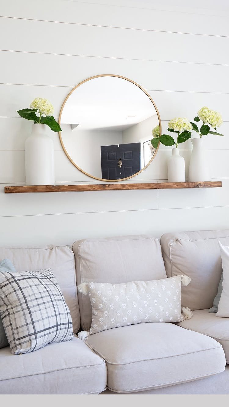 Wooden floating shelf with mirror and flowers mounted above a grey couch