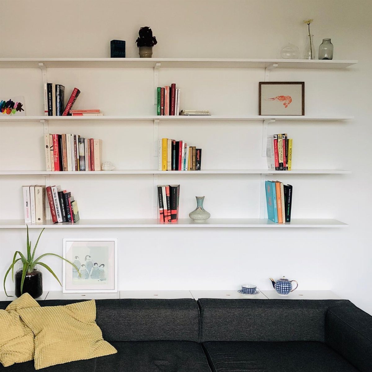 White floating shelves with books and decor above a dark grey couch