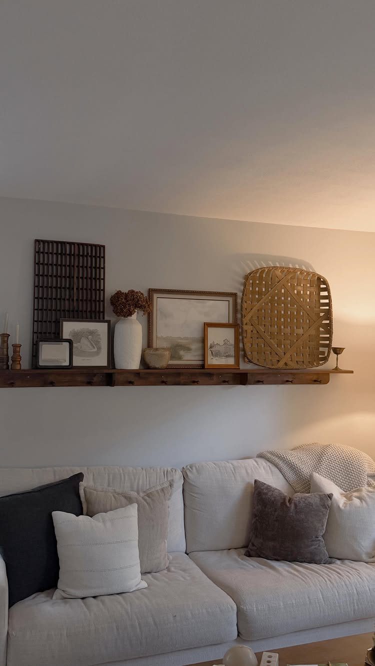Wooden floating shelf with decor mounted on a wall above a white couch