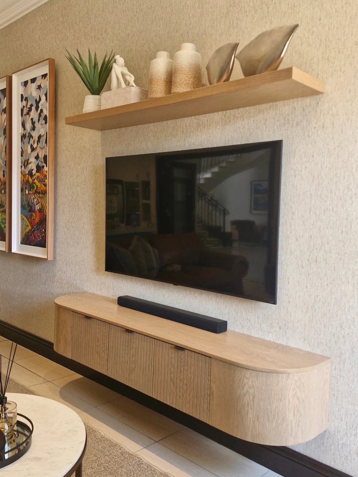 Flat-screen TV with light wood floating shelves above and below on a beige wall