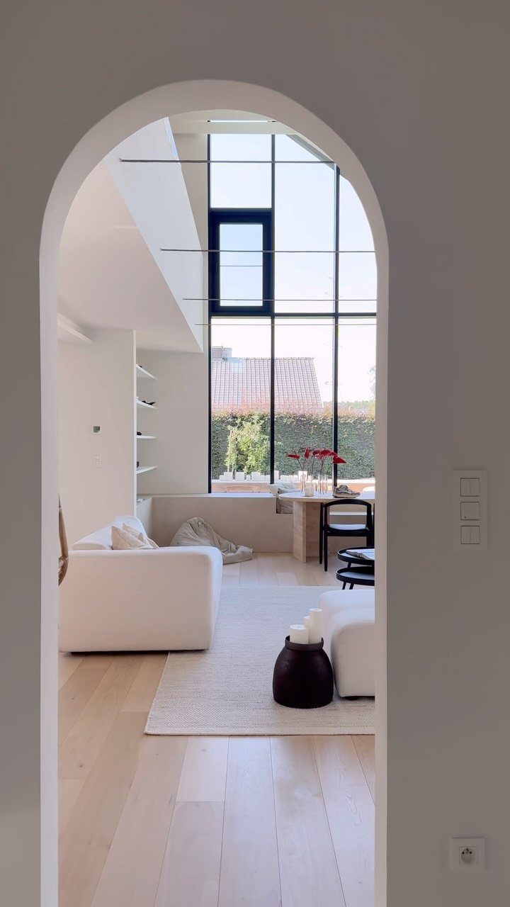 Bright living room with floor to ceiling windows seen through an arched doorway.