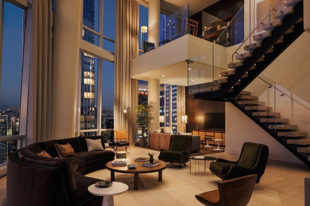 Luxury duplex apartment with floor to ceiling windows overlooking a city skyline at dusk