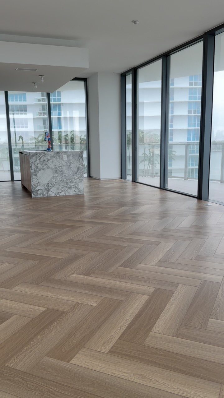 Modern apartment interior with herringbone wood floors and floor to ceiling glass windows.