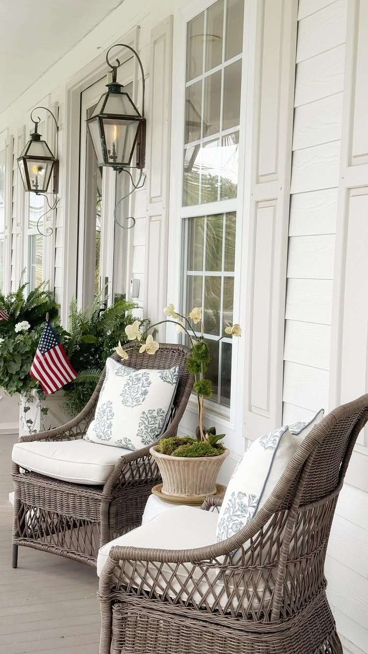 Wicker armchairs with white cushions and blue patterned pillows on a white porch.