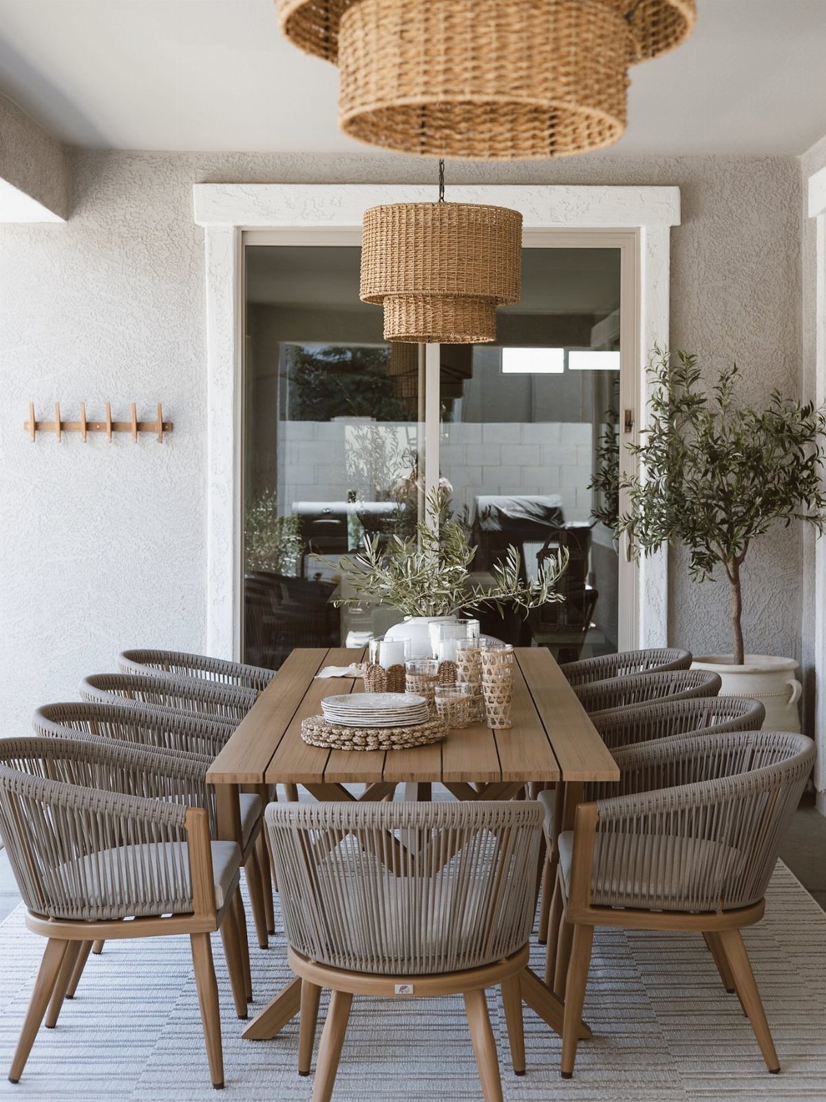 Wooden dining table and woven chairs on a neutral porch with pendant lights.