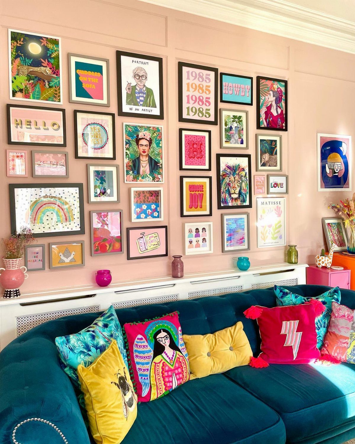 Teal velvet couch with colorful pillows under a gallery wall of framed art.