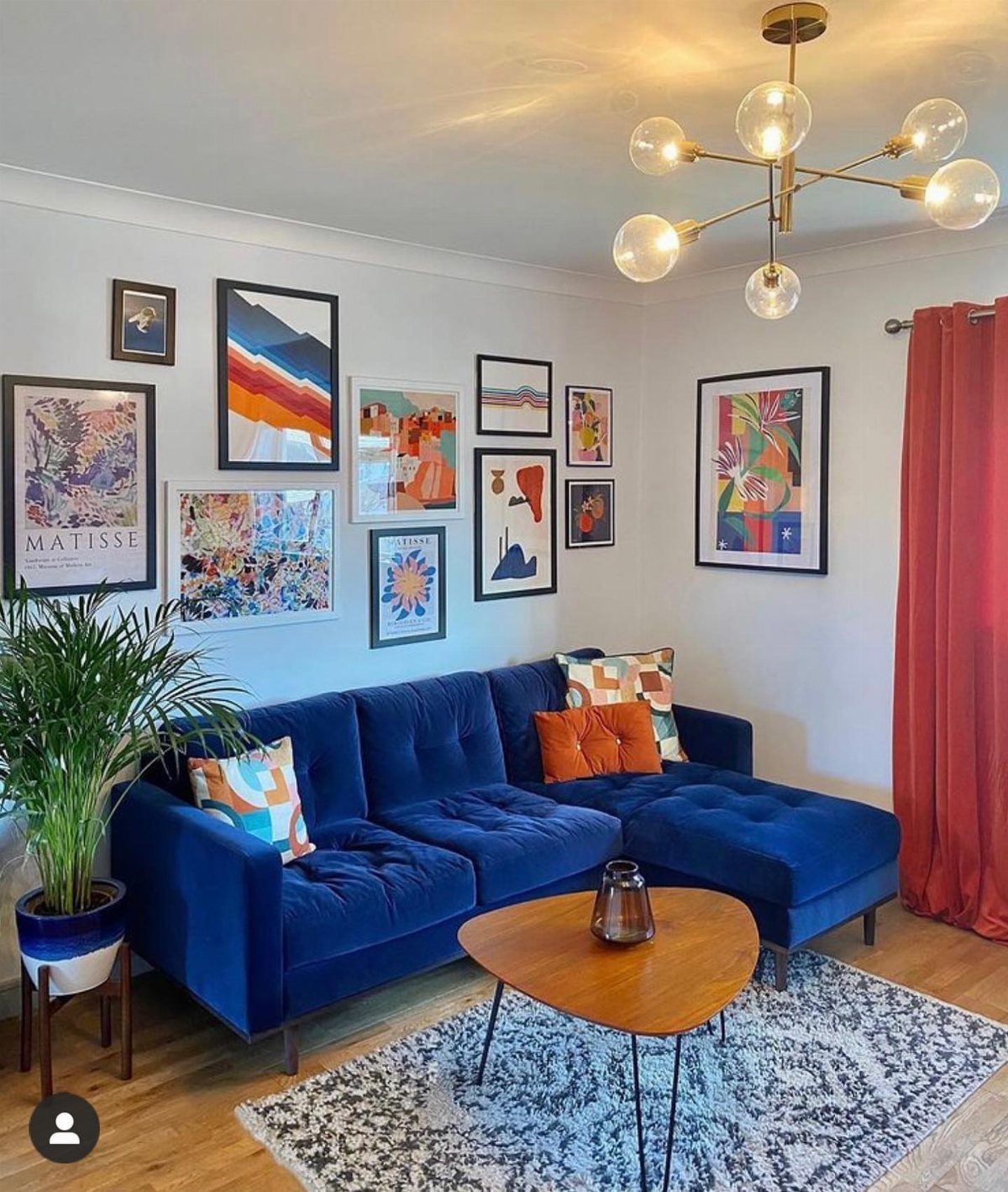Blue velvet sectional sofa under a gallery wall of colorful framed art prints.