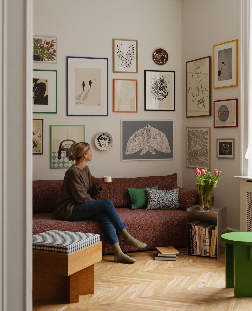 Woman sitting on a brown couch below a diverse gallery wall of art.
