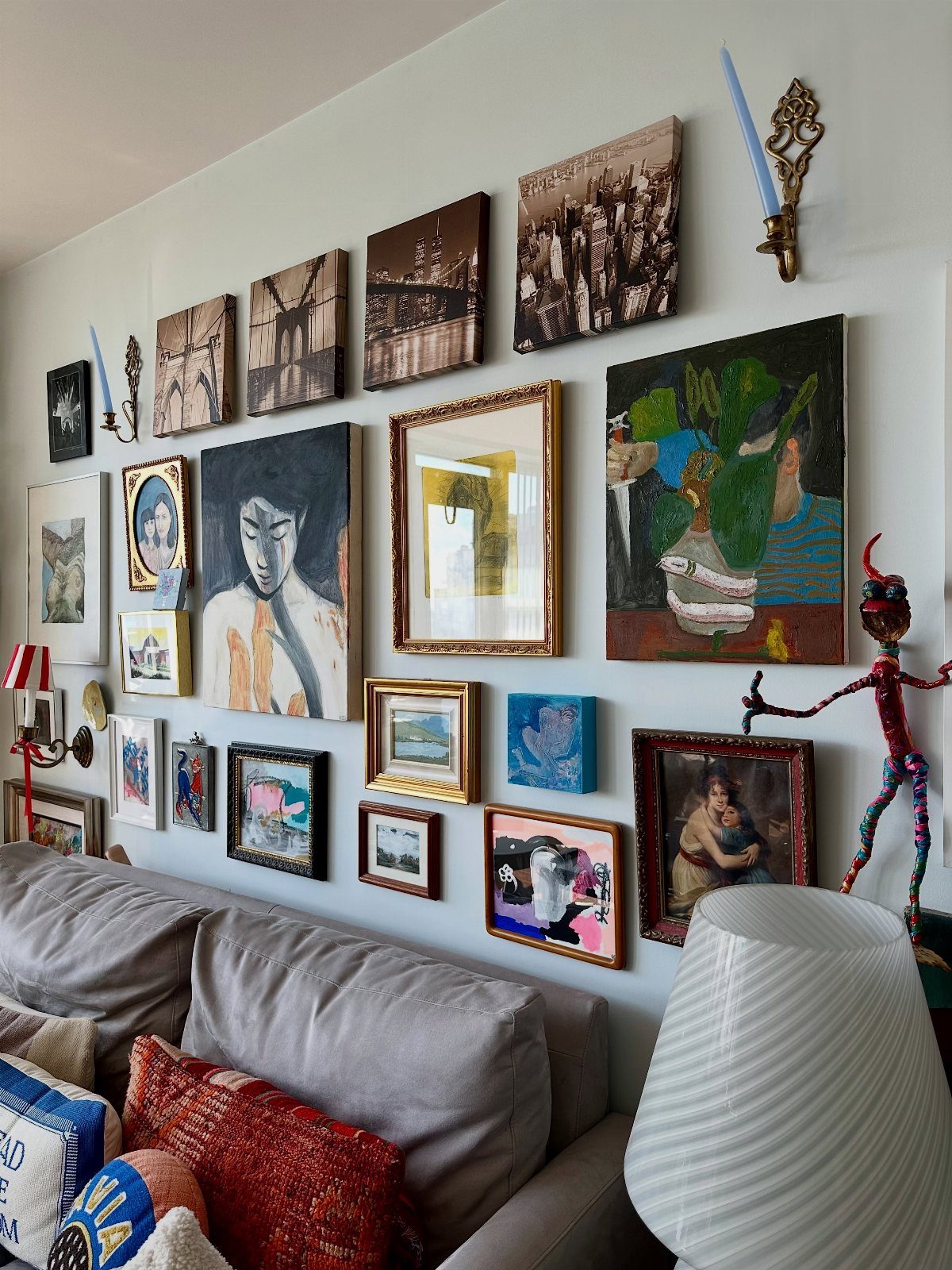 Gallery wall with diverse framed art and photos hanging above a grey couch.
