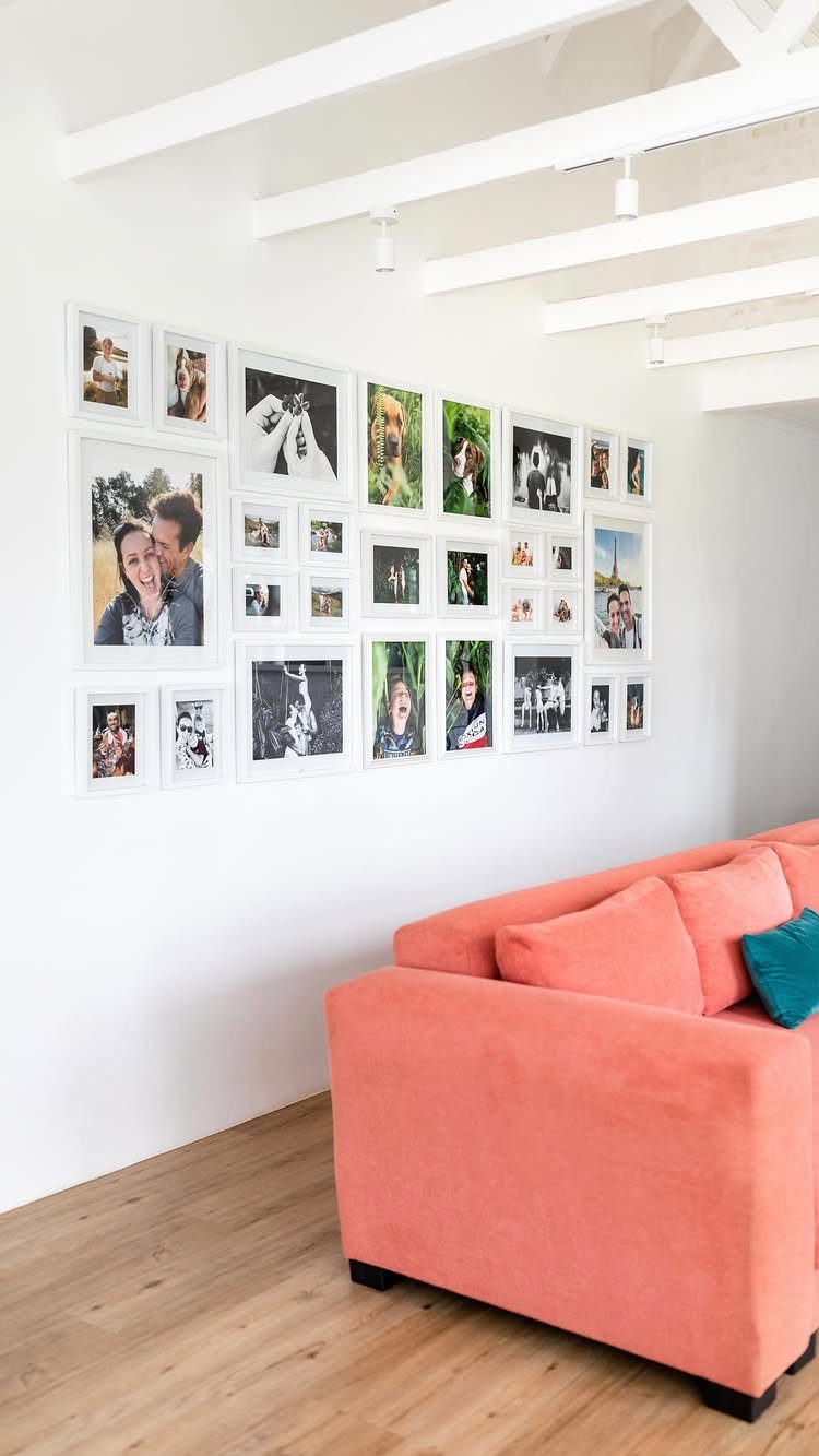 Gallery wall of white framed photos above a coral couch in bright room