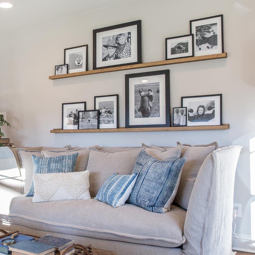 Wooden picture ledges with black framed photos above a beige couch with blue pillows