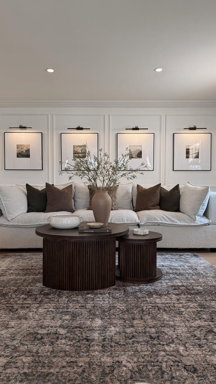 Four framed artworks with black picture lights hanging above a white modern couch.