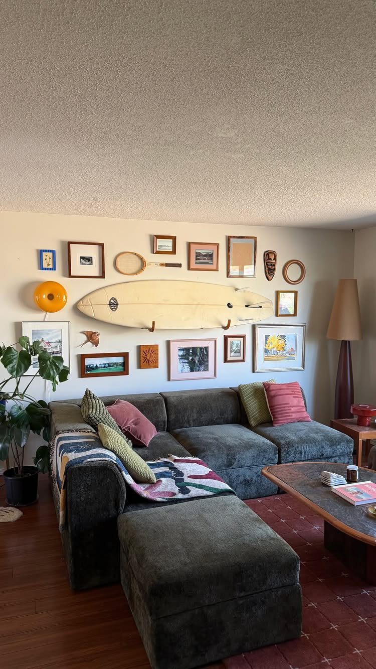 Gallery wall with a surfboard and framed art above a grey sectional sofa