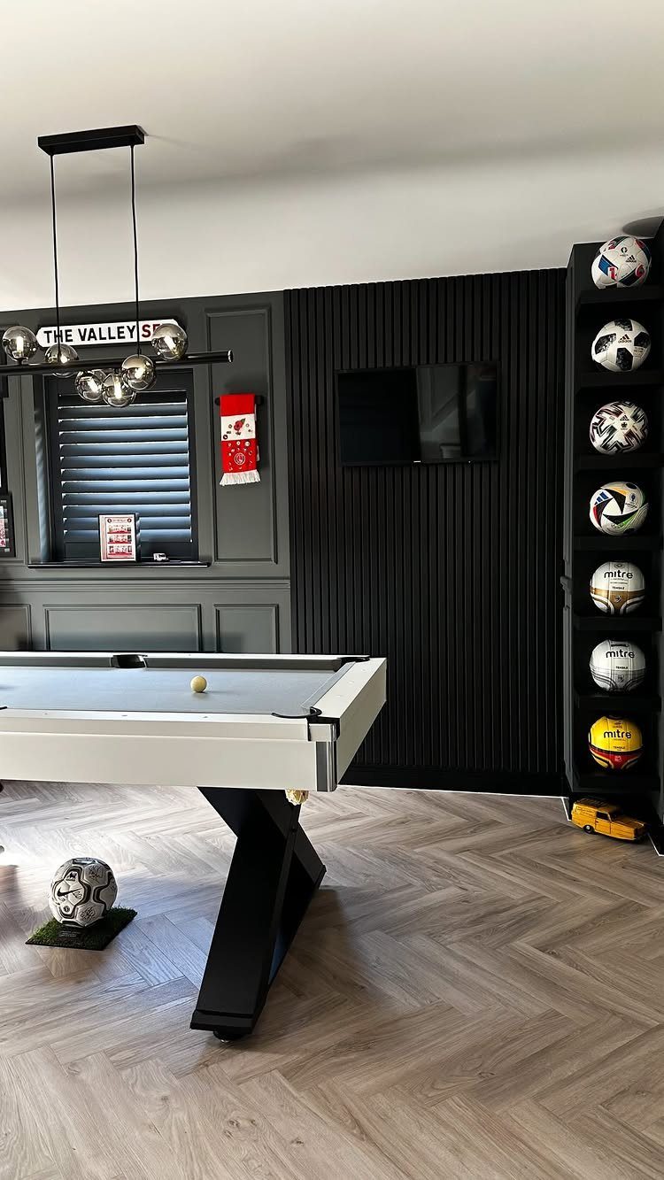 White pool table in a room with black slatted and grey paneled walls.