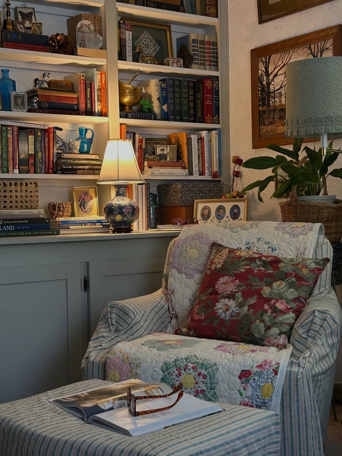 Striped armchair with floral quilt and pillow next to a crowded bookshelf.