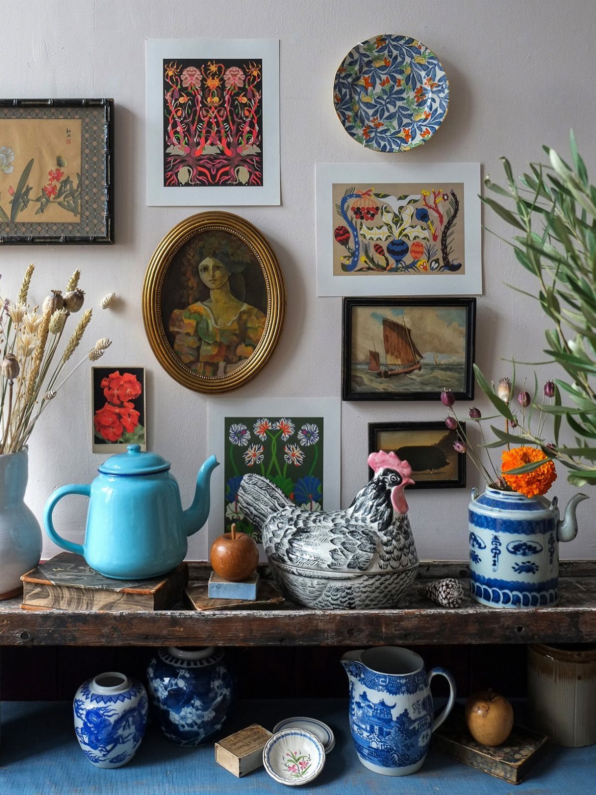 Eclectic wall gallery and wooden shelf with blue porcelain and vintage artwork.