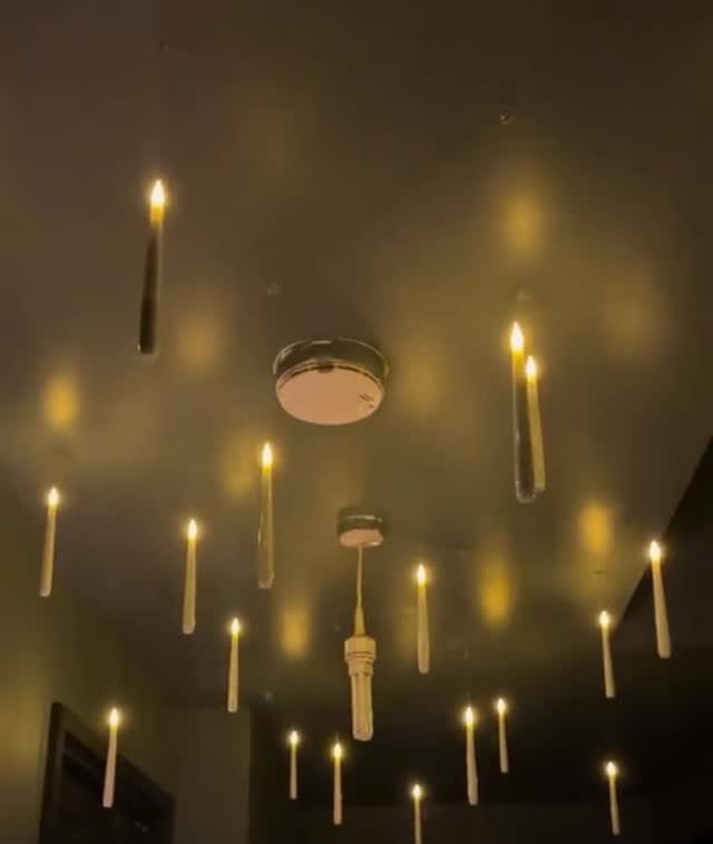 Floating white candles with glowing yellow flames hanging from a dark ceiling.