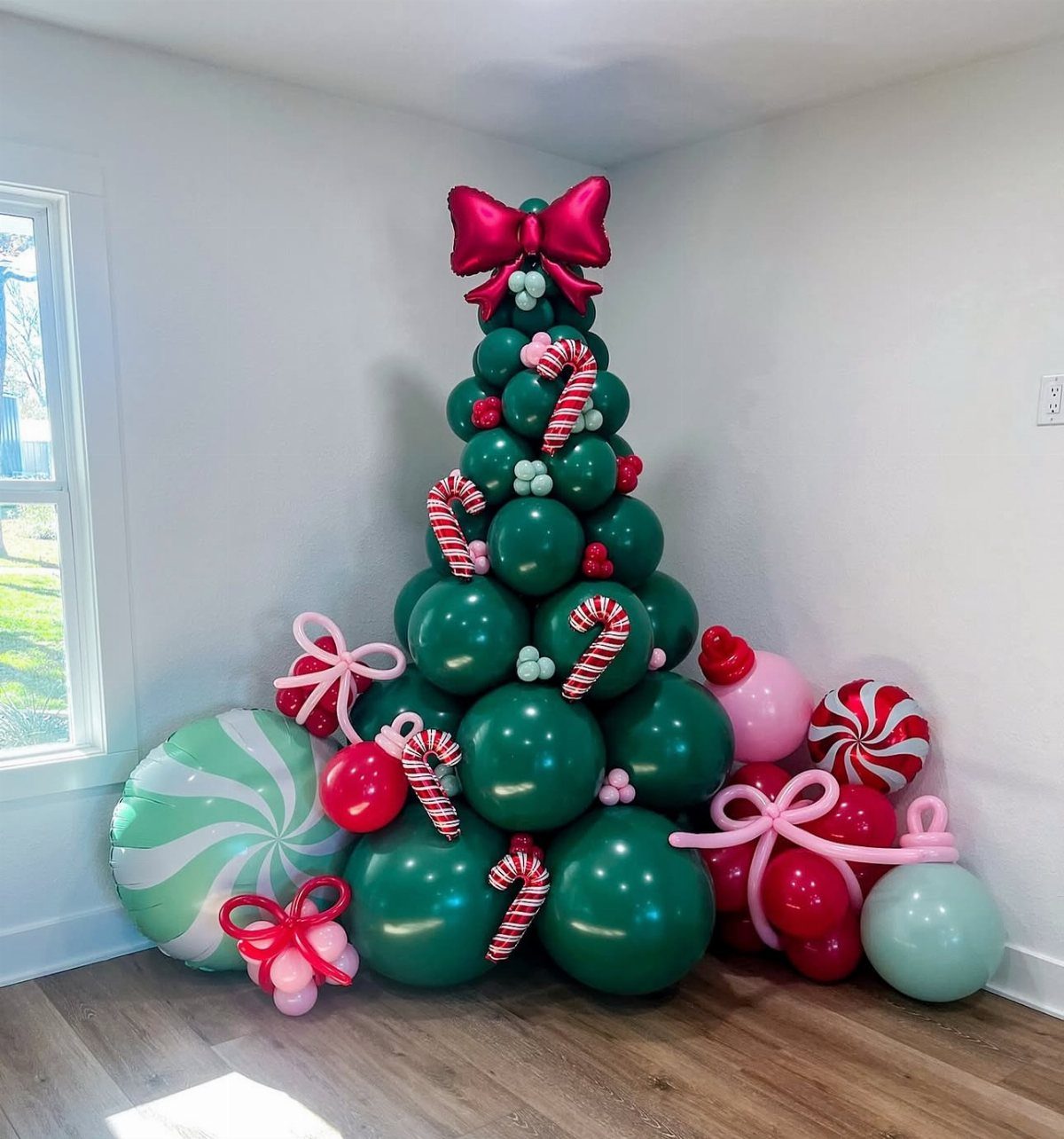 Balloon Christmas tree made of green balloons with candy cane accents and red bows.