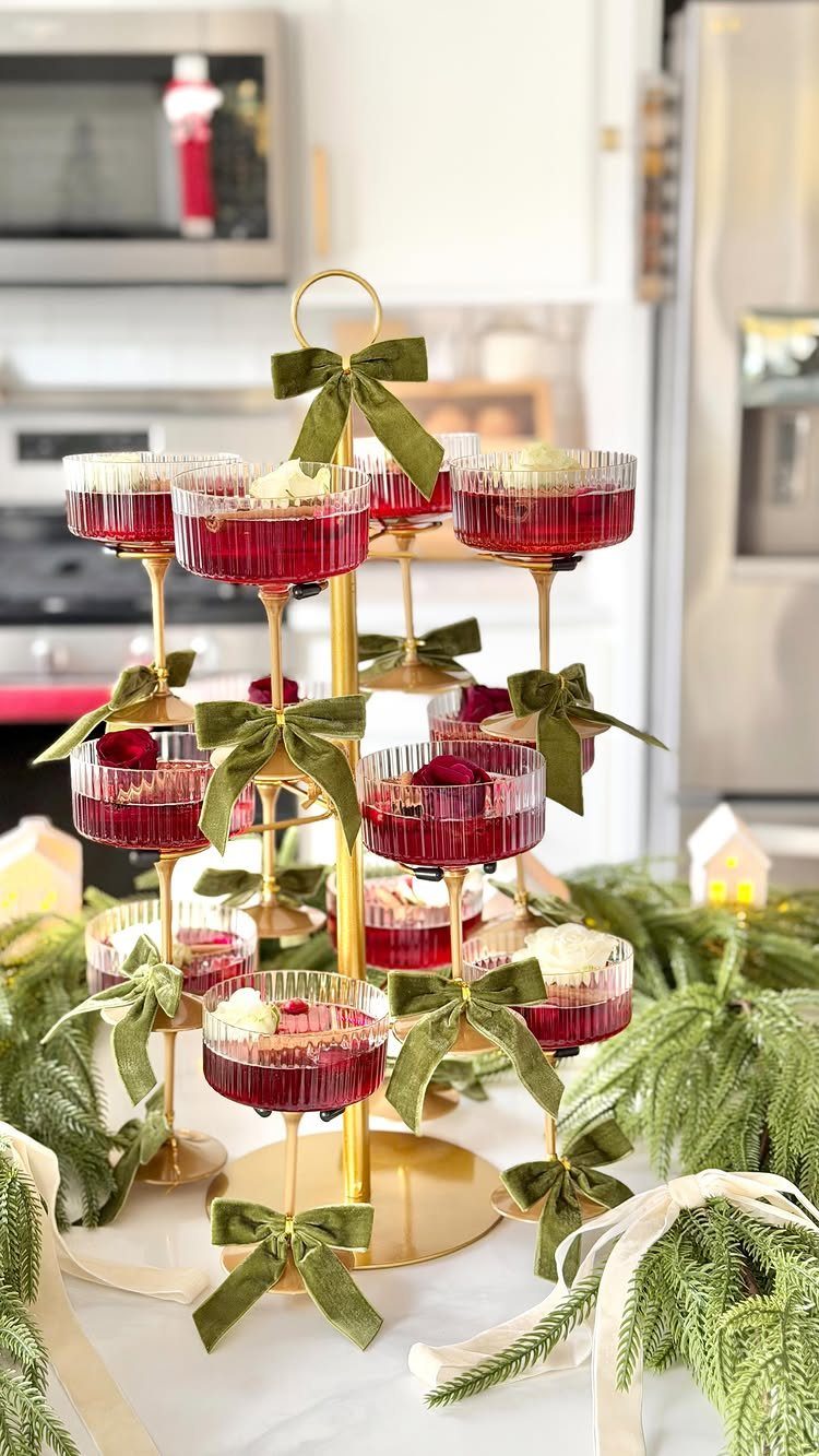 Gold tiered cocktail stand with red drinks and green velvet bows among evergreen branches.