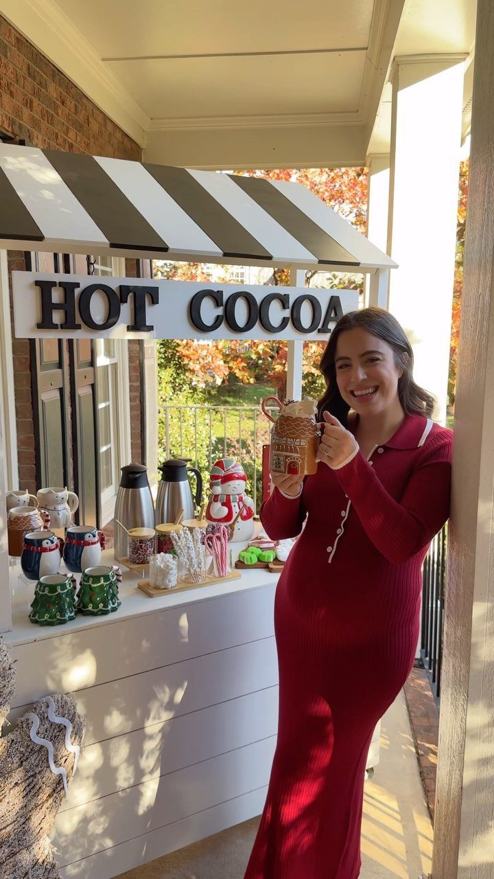 Woman in red dress posing by a festive outdoor hot cocoa bar station