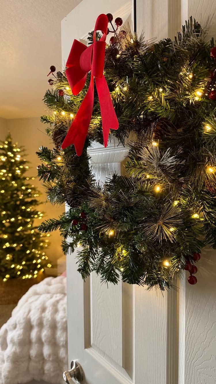 Green pine wreath with warm LED lights and red bow on white door