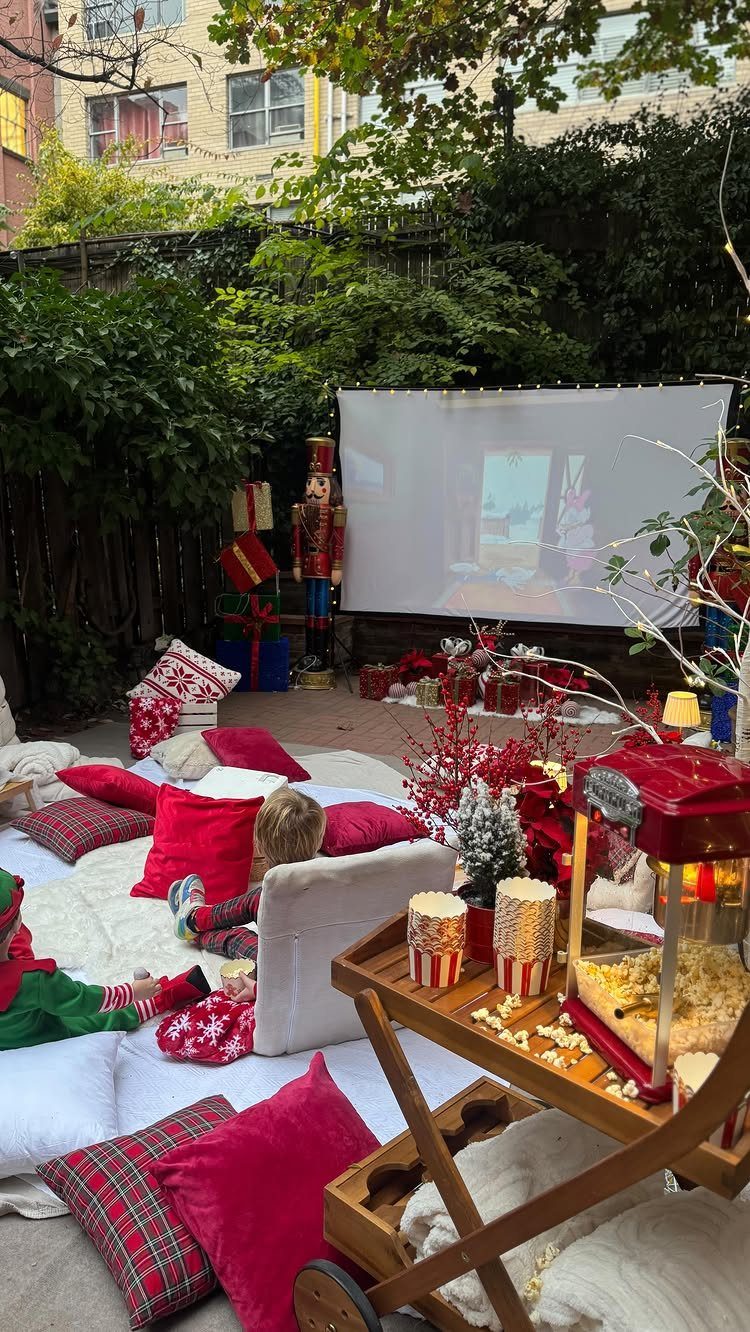 Outdoor holiday movie setup with projector screen, nutcracker, and popcorn on a cart.