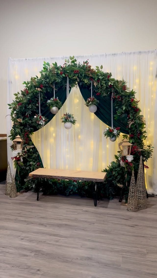 Circular greenery arch with red berries and white curtains for a photo backdrop.
